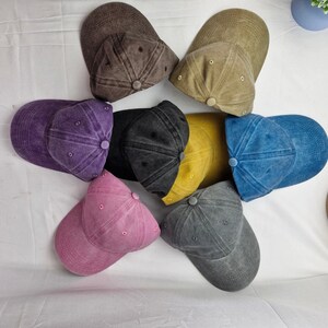K&ouml;nnte beinhalten: Sieben Baseballkappen in verschiedenen Farben. Die Kappen sind aus weichem, strukturiertem Stoff. Die Farben sind lila, braun, gelb, blau, rosa, grau und beige.