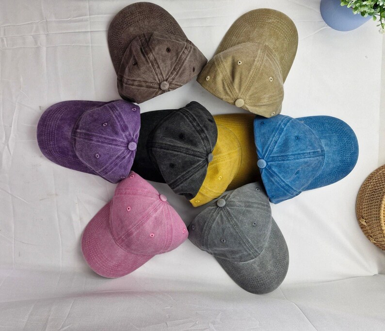 K&ouml;nnte beinhalten: Sieben Baseballkappen in verschiedenen Farben. Die Kappen sind aus weichem, strukturiertem Stoff. Die Farben sind lila, braun, gelb, blau, rosa, grau und beige.