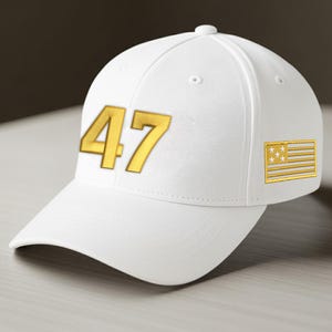 May include: A white baseball cap featuring the number "47" in gold. A gold and white flag patch is on the side. The cap has a curved peak and a button on top.