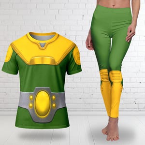 May include: A short-sleeved green t-shirt and matching green leggings featuring a printed yellow chest plate, yellow shoulder pads, a silver belt with a central yellow oval buckle, and yellow knee pads with horizontal line detailing.
