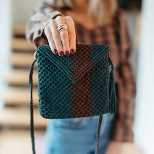 May include: A small, dark green and brown crocheted crossbody bag with a tassel. The bag has a woven design and a long strap.