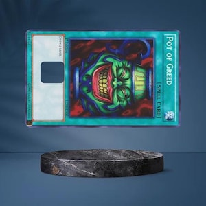 May include: A Yu-Gi-Oh! "Pot of Greed" spell card, featuring a grinning green face with red and yellow details, floats above a dark, circular platform. The card has a teal border and text that reads "Draw 2 cards."
