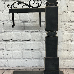 May include: A black wooden display stand with a rectangular base, a vertical post, and a horizontal arm featuring a decorative scrollwork top. The structure has distressed edges and a flat, matte finish, designed to hold items from the hanging hooks.