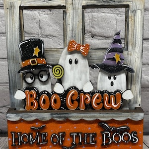 May include: A Halloween-themed wooden decoration featuring three white ghost figures. One ghost wears a top hat, another a bow, and the third a witch hat. The words "Boo Crew" and "Home of the Boos" are displayed in orange lettering.