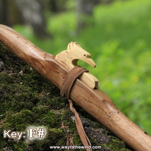 Könnte beinhalten: Eine indianische Flöte aus Holz mit einer Vogelgravur auf der Oberseite. Die Flöte ist braun und hat eine natürliche Holzoptik. Die Tonart der Flöte ist F#. Die Flöte liegt auf einem moosbewachsenen Baumstamm.