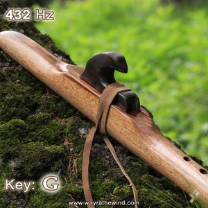 May include: A wooden Native American flute with a carved bird head on the top. The flute is brown and has a leather strap attached to it. The text "432 Hz" and "Key: G" is visible in the image.