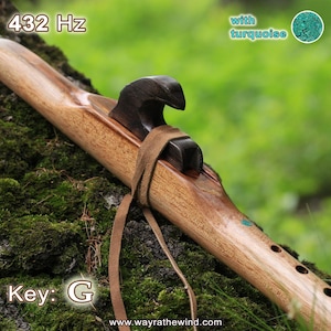 Può includere: Un flauto nativo americano in legno con accenti turchesi. Il flauto è appoggiato su un letto di muschio e ha una tonalità di G. Il testo "432 Hz" è visibile sul flauto.