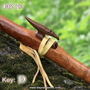 Op de afbeelding: Een houten Native American fluit met een gegraveerd vogelhoofd aan het uiteinde. De fluit is bruin en heeft een natuurlijke houtkleur. De fluit is vastgebonden met een lichtbruine leren riem. De tekst "432 Hz" en "Key: D" is zichtbaar in de afbeelding.