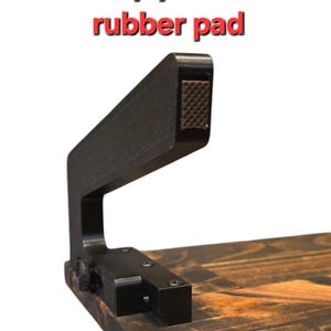 May include: A black metal anti-slip protective rubber pad with a textured surface. The pad is attached to a wooden surface with screws.