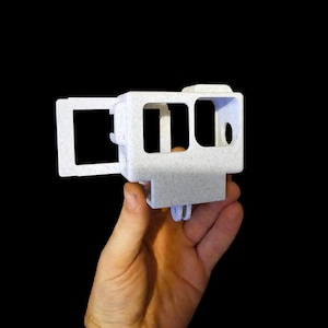 May include: White plastic camera case with a textured finish. The case has a hinged door on the side and a mount on the bottom.