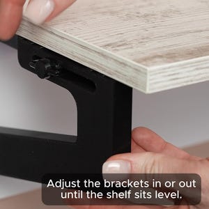 May include: A close-up of a black metal shelf bracket being adjusted to level a wooden shelf. The text "Adjust the brackets in or out until the shelf sits level." is visible in the image.