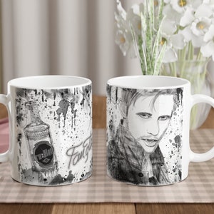 Puede incluir: Dos tazas de cerámica blanca con ilustraciones en blanco y negro. Una taza presenta una ilustración en blanco y negro de un hombre con una botella de alcohol. La otra taza presenta una ilustración en blanco y negro de un hombre con una expresión seria. Ambas tazas tienen salpicaduras de pintura negra en el fondo.