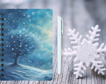 May include: A spiral-bound notebook featuring a blue winter landscape with a bare tree and falling snowflakes on the cover, accompanied by a plain white ballpoint pen and a large, textured white snowflake ornament.