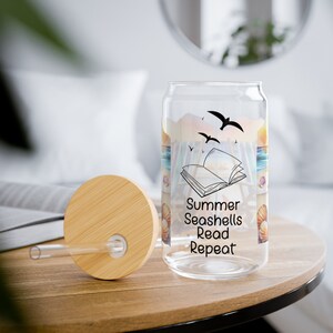 May include: A clear glass reusable water bottle with a bamboo lid and straw. The bottle has a beach scene with seashells and a book printed on it. The text on the bottle reads "Summer Seashells Read Repeat".