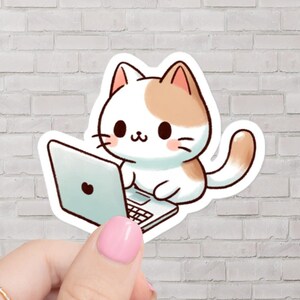 以下が含まれることがあります： 大きな目とピンクの鼻をした白と茶色の猫が、ラップトップコンピューターに座っています。猫は白いシャツを着て、茶色の尻尾をしています。