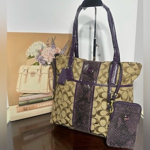 May include: Tan and purple Coach tote bag with matching wallet. The tote features a repeating logo pattern with purple accents and a snakeskin-like stripe down the center. The wallet has a similar design. The bag has a top handle.