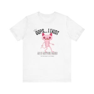 May include: White t-shirt featuring a cartoon creature with the text "OOPS... I EXIST" above the creature and "AS IF ANYONE CARES" below. The creature is pink with red ears and eyes.