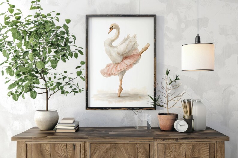 May include: A framed watercolour print of a swan in a ballet pose, wearing a pink tutu. The artwork is displayed on a wooden cabinet, with potted plants and decorative items. The swan is depicted with delicate brushstrokes.