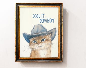 May include: Framed artwork featuring a watercolor illustration of a cat wearing a blue cowboy hat. The text "COOL IT, COWBOY" is written above the cat. The frame is black with gold trim.