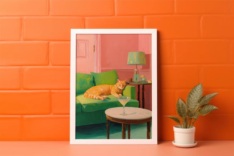 May include: A framed painting shows an orange tabby cat resting on a green sofa. A martini glass is on a small table in front of the sofa. The room has a pink wall and a green lamp.