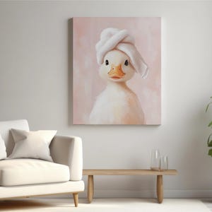 May include: A canvas print featuring a charming duckling wearing a white towel on its head. The duckling has a yellow beak and is set against a soft pink background. The artwork is displayed in a modern living room setting.