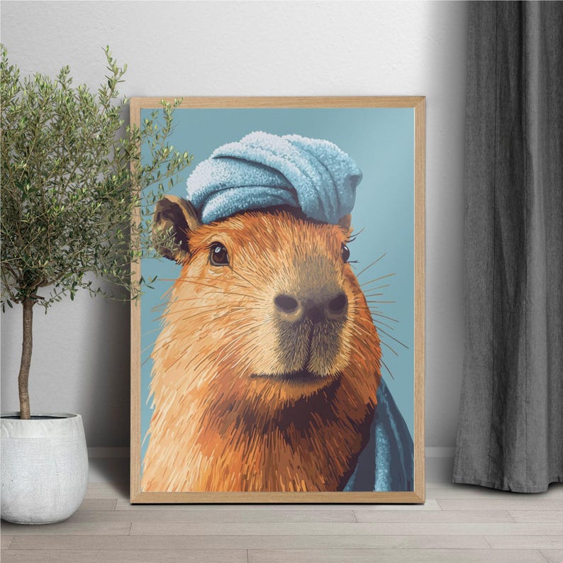May include: A framed art print featuring a capybara wearing a blue towel on its head. The capybara has brown fur and is set against a light blue background. The artwork is in a wooden frame.