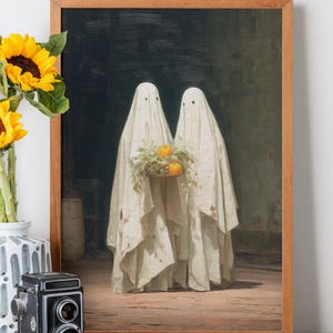 May include: A framed print featuring two figures draped in white sheets, resembling ghosts, holding a tray of oranges and greenery. The artwork has a vintage aesthetic, with a dark background and wooden frame. Sunflowers and a vintage camera are in the foreground.