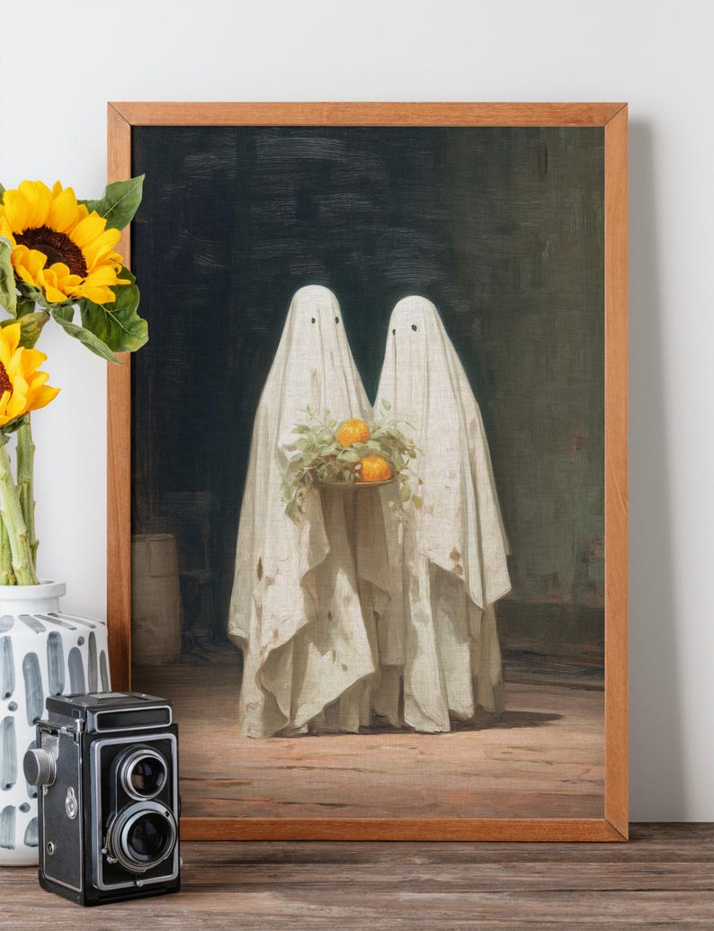 May include: A framed print featuring two figures draped in white sheets, resembling ghosts, holding a tray of oranges and greenery. The artwork has a vintage aesthetic, with a dark background and wooden frame. Sunflowers and a vintage camera are in the foreground.