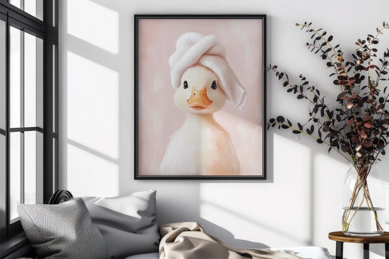 May include: A framed print featuring a charming duckling wearing a white towel on its head. The duckling has a yellow beak and is set against a soft pink background. The artwork is displayed in a black frame.