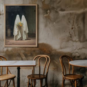 May include: A framed artwork depicts two figures draped in white fabric, holding a bouquet of yellow flowers. The painting hangs on a textured wall, with wooden chairs and tables in the foreground, creating a vintage cafe setting.