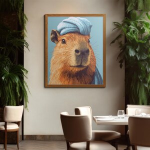 May include: A framed art print featuring a capybara wearing a blue turban and scarf. The capybara has brown fur and a light blue background. The artwork is displayed in a restaurant setting with tables and chairs.