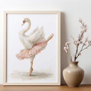 May include: A framed watercolour print of a swan in a ballet pose, wearing a pink tutu and pointe shoes. The artwork is displayed on a wooden surface next to a vase with pink flowers. The swan is depicted with white feathers and a curved neck.