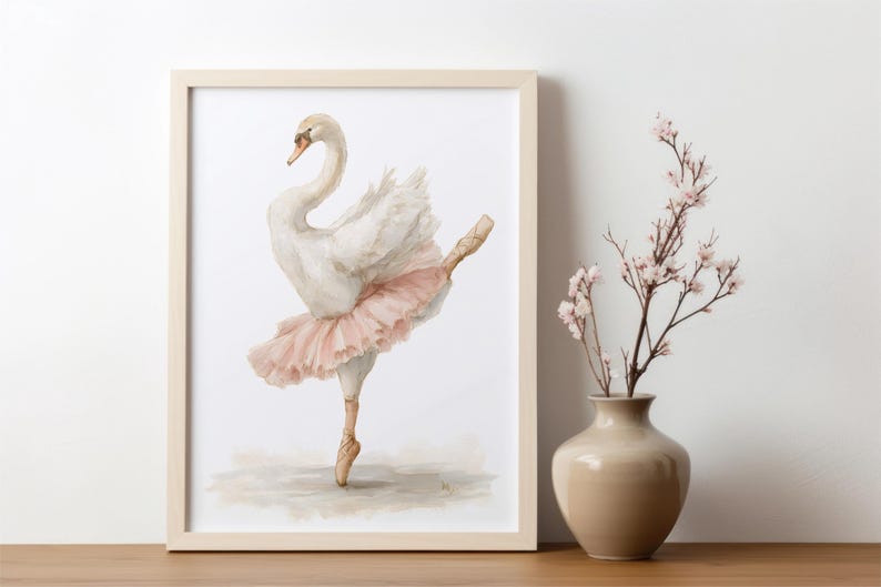 May include: A framed watercolour print of a swan in a ballet pose, wearing a pink tutu and pointe shoes. The artwork is displayed on a wooden surface next to a vase with pink flowers. The swan is depicted with white feathers and a curved neck.