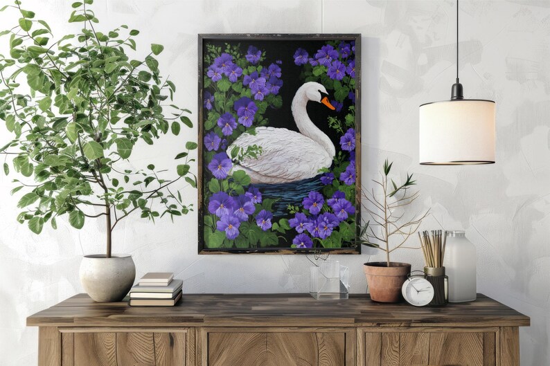 Op de afbeelding: Een ingelijst schilderij van een witte zwaan met een oranje snavel, omringd door paarse bloemen en groene bladeren. Het kunstwerk wordt tentoongesteld op een houten kast, met een plant en andere decoratieve items.