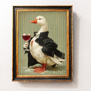 Op de afbeelding: Ingelijst kunstwerk met een witte eend in een zwarte smoking, die een glas rode wijn vasthoudt. De eend heeft een oranje snavel en poten. De achtergrond is lichtgroen met verticale strepen. De lijst is zwart en goud.