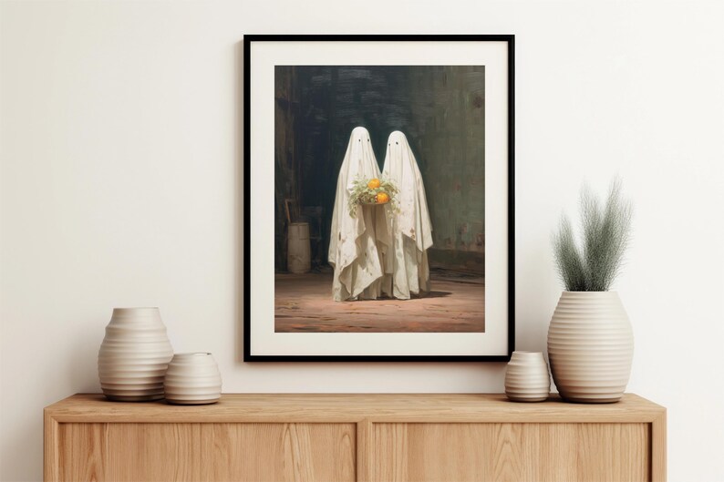 May include: Framed art print featuring two figures draped in white sheets, resembling ghosts, holding a bouquet of orange flowers. The artwork has a vintage aesthetic, set against a dark, moody background.