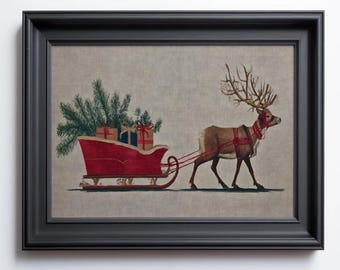 May include: Framed artwork featuring a reindeer pulling a red sleigh filled with wrapped gifts and evergreen branches. The reindeer has large antlers and is harnessed to the sleigh with red straps. The artwork is set against a neutral background and framed in black.
