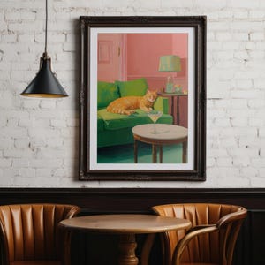 May include: A framed art print shows an orange cat on a green sofa, with a martini on a table. The artwork is set in a room with pink walls and a green lamp. The print is displayed on a white brick wall.