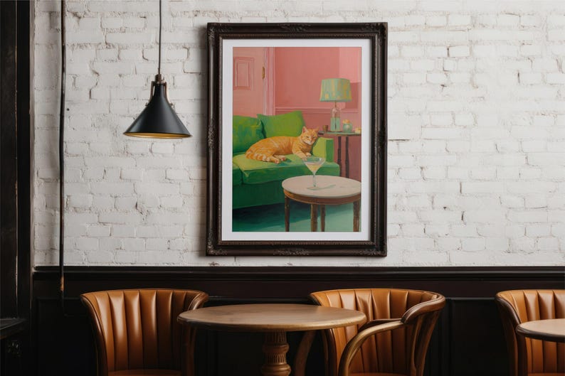 May include: A framed art print shows an orange cat on a green sofa, with a martini on a table. The artwork is set in a room with pink walls and a green lamp. The print is displayed on a white brick wall.
