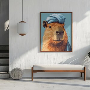 May include: A framed art print featuring a capybara wearing a blue turban. The capybara has brown fur and is set against a light blue background. The artwork is displayed in a modern interior setting.