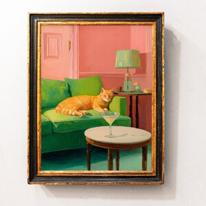 May include: A framed painting shows an orange tabby cat resting on a green sofa. A martini glass is on a small round table. The room has pink walls and a green lamp. The painting is in a black and gold frame.