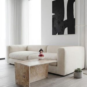 May include: A contemporary living room with a cream-coloured sectional sofa, a rectangular stone coffee table, and a black and white abstract artwork. A small succulent in a grey pot and a figurine are also present.
