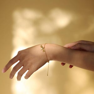 Peut inclure: Un bracelet en chaîne dorée avec un délicat charme en forme de nœud. Le bracelet est porté au poignet.