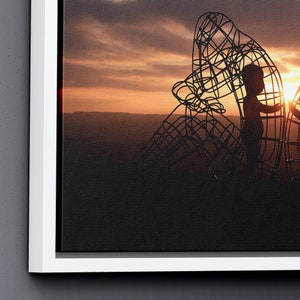 May include: Silhouette of a child standing inside a large metal sculpture against a sunset sky.