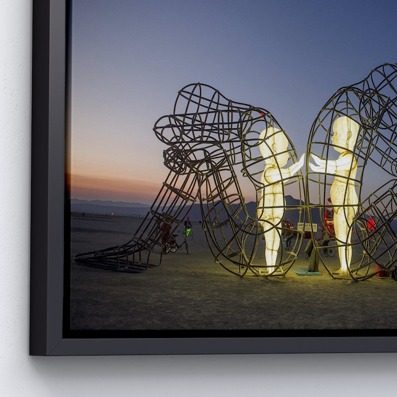 Pu&ograve; includere: Una grande scultura in metallo di due figure che si tengono per mano, illuminate dall'interno, su uno sfondo di paesaggio desertico al tramonto.