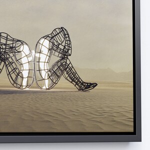 May include: A black metal sculpture of two figures sitting back to back in a desert landscape. The figures are made of a wire mesh and are partially transparent, revealing a white light inside.