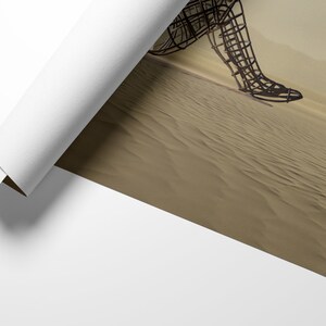 May include: A wire sculpture of a person walking across a sandy desert. The sculpture is made of metal and is in a rusted brown color. The desert is a light brown color and the sand is textured.