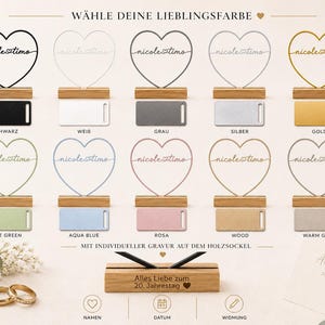 May include: A collection of ten heart-shaped wire ornaments in various colors, each mounted on a wooden base. The hearts feature the text nicole timo. Below, a wooden base displays the engraved text Alles Liebe zum 20. Jahrestag with a heart icon.