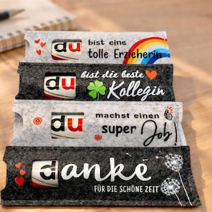 May include: Four rectangular felt sleeves in light and dark gray, each holding a chocolate bar with the visible text 'du'. The sleeves feature printed German phrases, a rainbow, a clover, a thumbs-up icon, hearts, and dandelion illustrations.