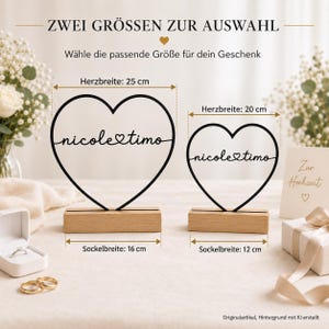 May include: Two black heart-shaped wire sculptures with the text nicole and timo connected by a heart symbol. Each heart sits on a rectangular wooden base. The larger heart is 25 cm wide with a 16 cm base, and the smaller is 20 cm wide with a 12 cm base.
